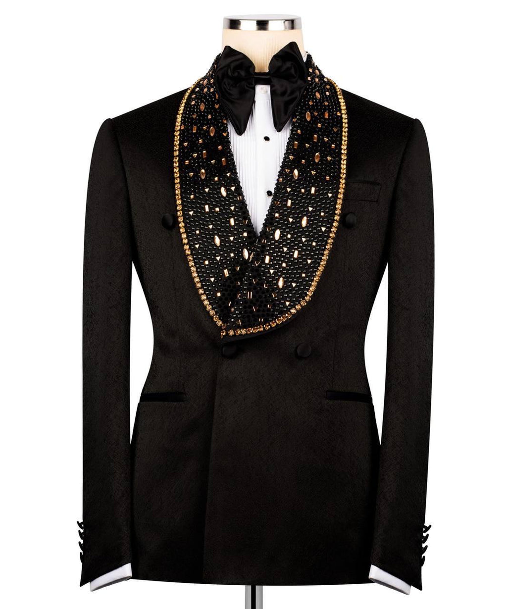 A black double-breasted tuxedo jacket with a wide shawl collar embellished with black beads and gold trim, styled with a black bow tie and white dress shirt on a mannequin.