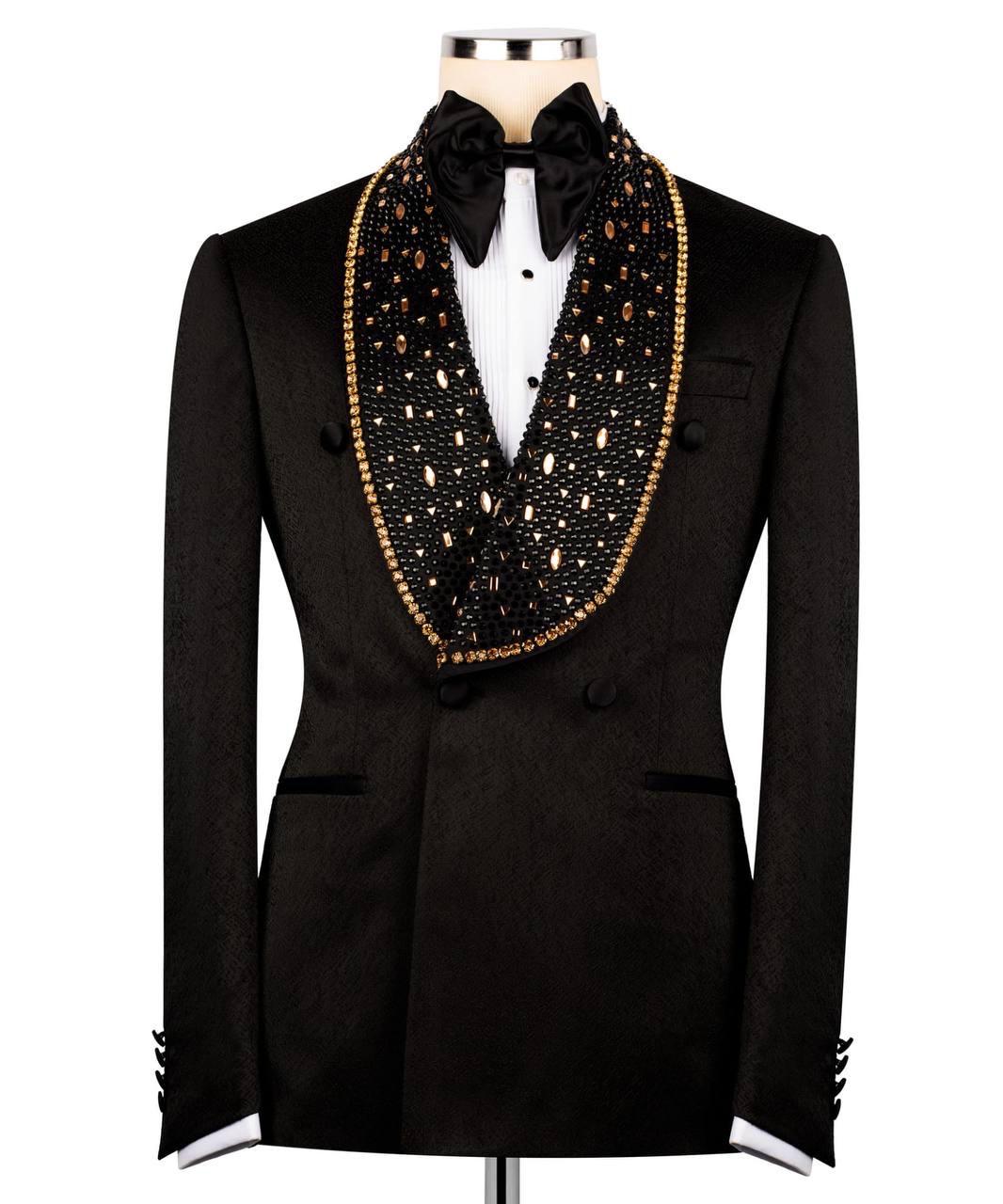 A black double-breasted tuxedo jacket with a wide shawl collar embellished with black beads and gold trim, styled with a black bow tie and white dress shirt on a mannequin.