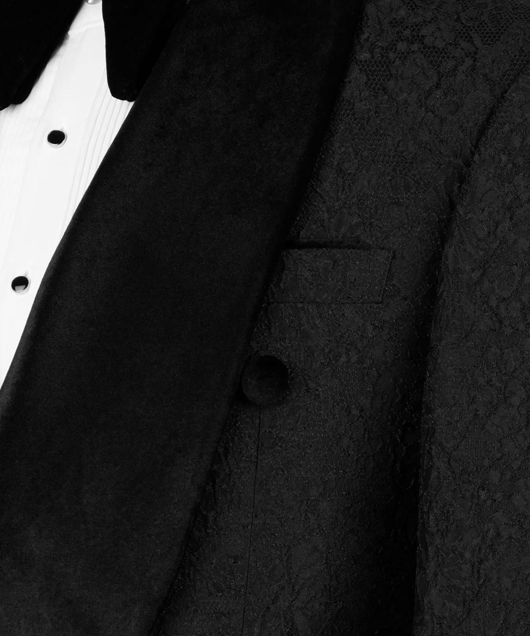 Close-up of a black textured tuxedo jacket with a satin peak lapel and a white pleated tuxedo shirt.