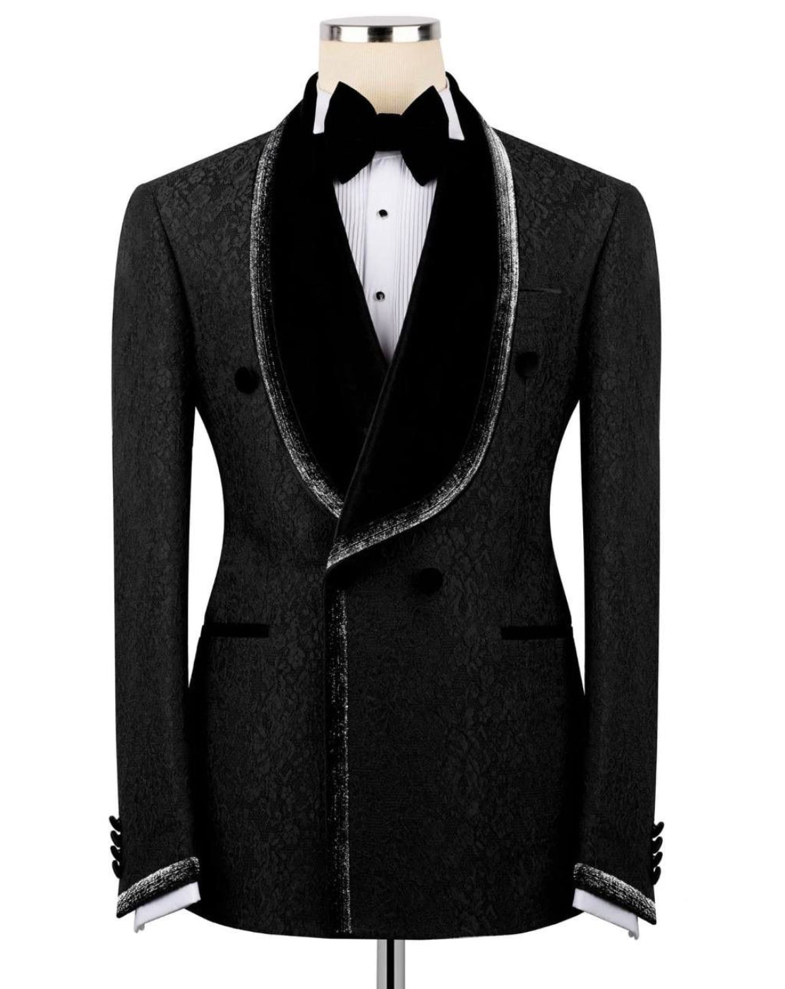 A men's black double-breasted tuxedo jacket with a textured pattern, black velvet shawl collar, and silver trim, displayed on a mannequin with a white shirt and black bow tie.
