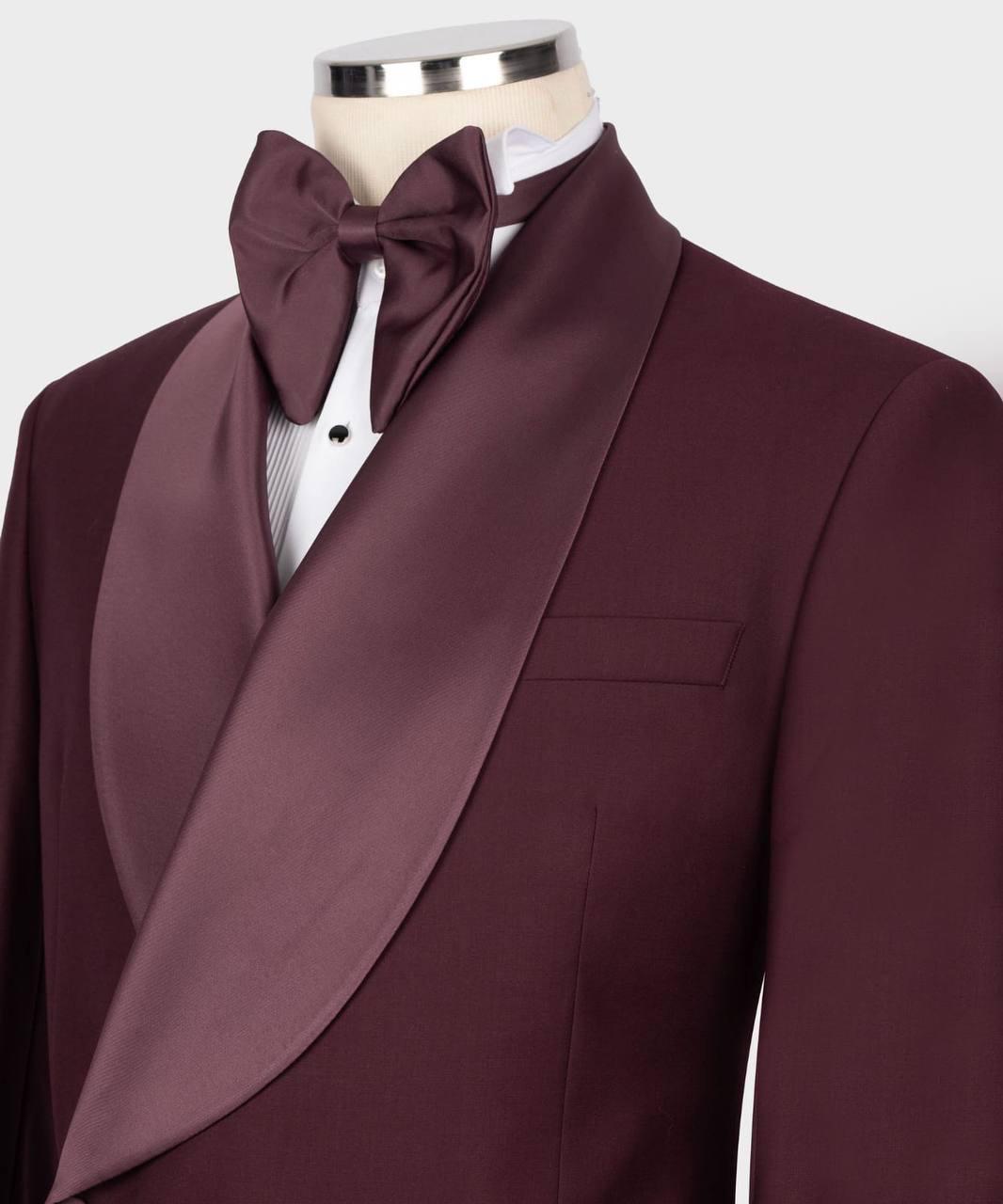 A men's formalwear set on a mannequin torso, featuring a deep burgundy satin shawl-collar tuxedo jacket, matching bow tie, white dress shirt, and a thin gray striped tie.