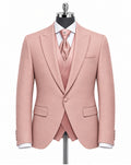 A men's three-piece suit in dusty pink, displayed on a black mannequin torso. The set includes a single-breasted blazer with peak lapels, a matching vest, a matching tie, a white dress shirt, and a white pocket square.