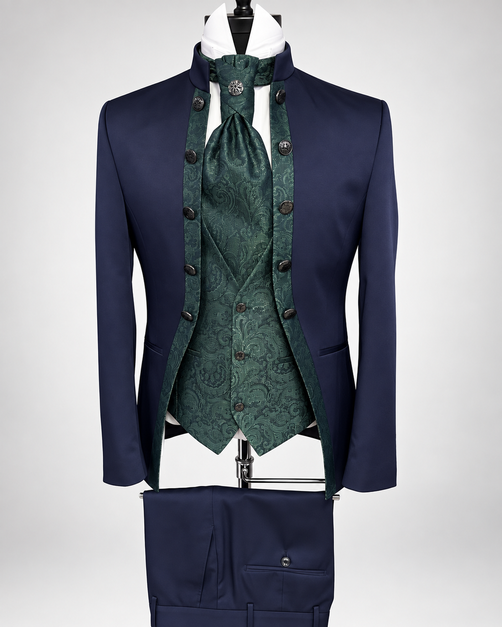 A formal men's suit displayed on a mannequin against a light gray studio background. The outfit includes a navy blue jacket and matching trousers, with a dark green patterned waistcoat, matching necktie, and white shirt visible at the collar.