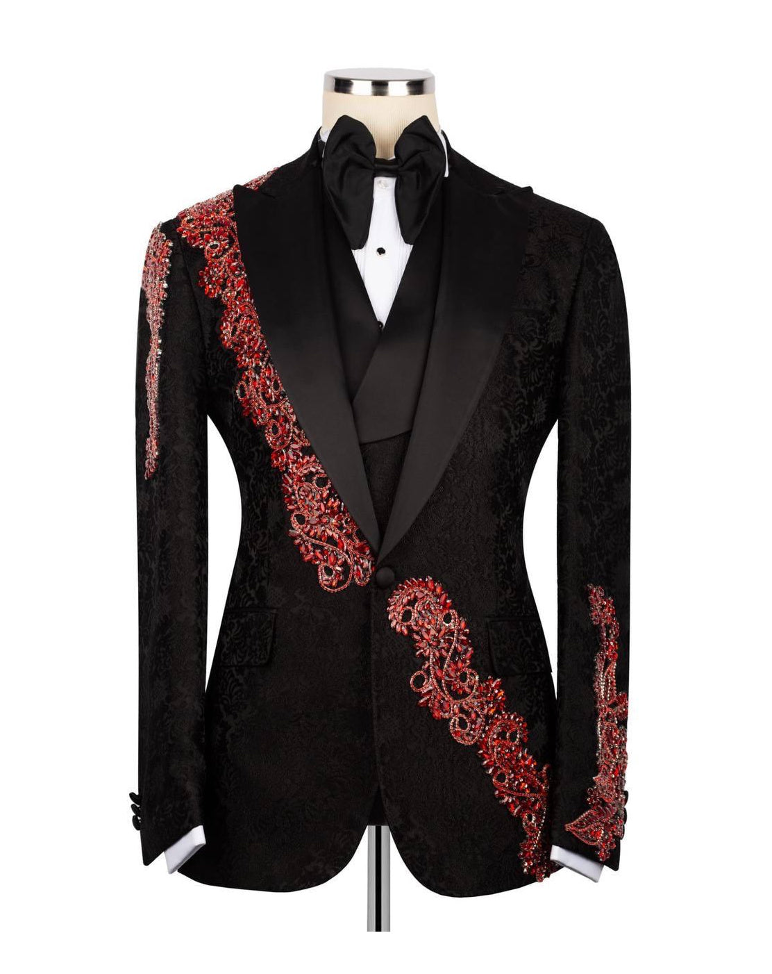 A black tuxedo jacket with red embroidered detailing, displayed on a mannequin with a black bow tie and white shirt.