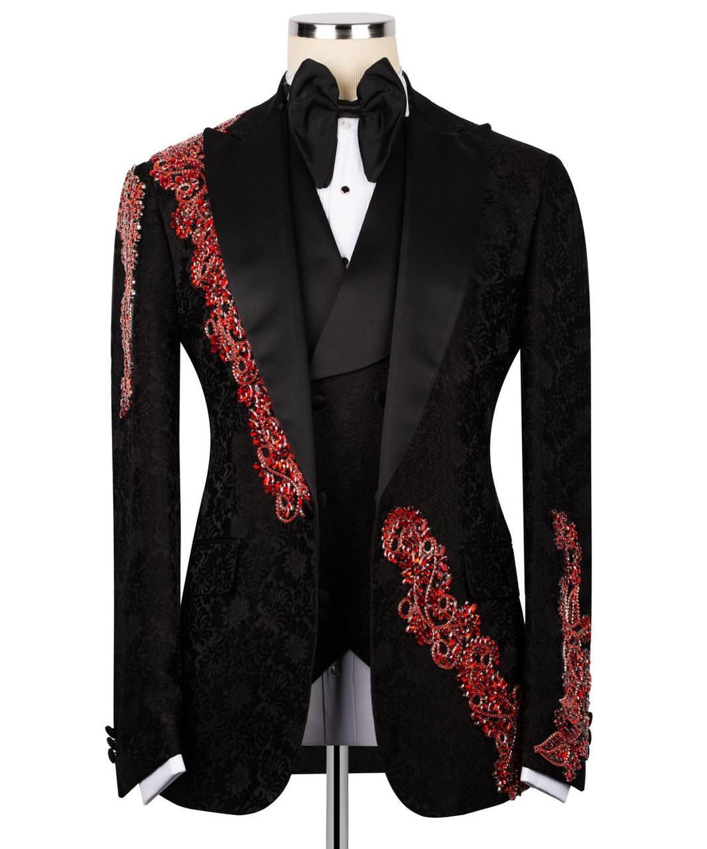 A black tuxedo jacket with ornate red embroidered detailing on the lapels and sleeves, displayed on a mannequin with a black bow tie and white shirt.