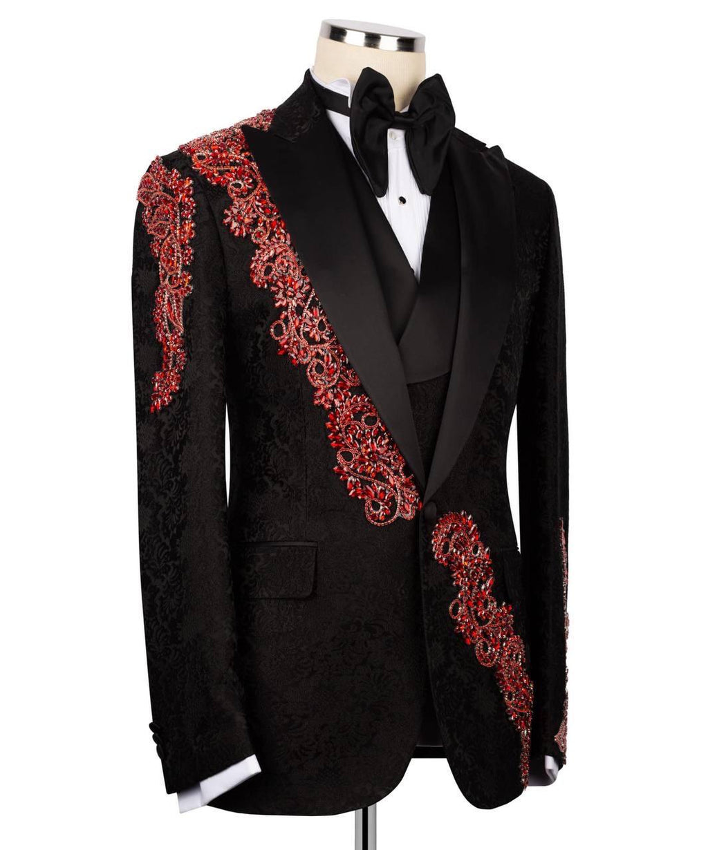 A black tuxedo jacket with ornate red and gold embroidered patterns along the lapels and shoulders, displayed on a mannequin with a black bow tie and white shirt.