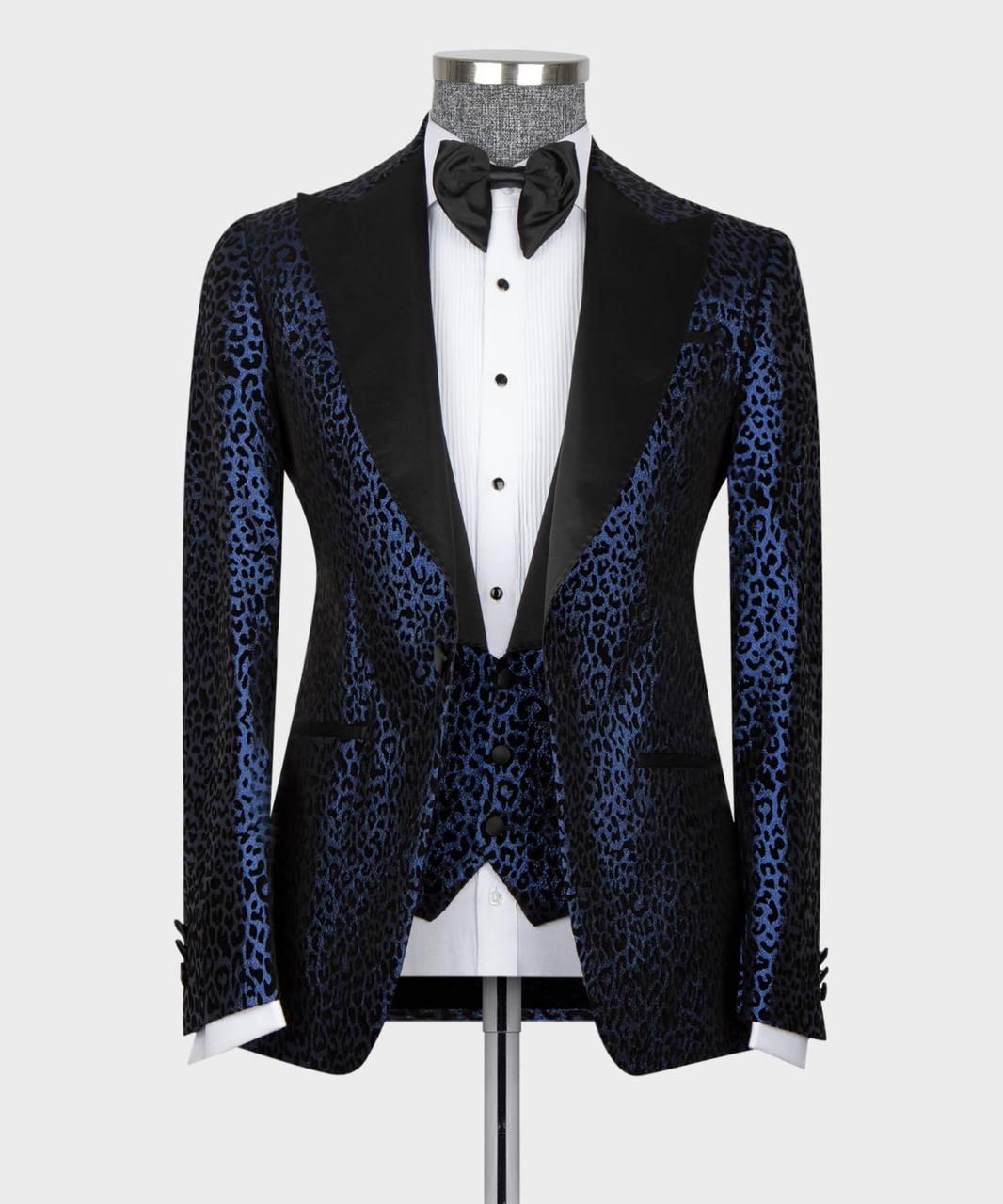 A men's tuxedo jacket displayed on a mannequin torso, featuring a blue and black leopard print satin body with contrasting black satin lapels, paired with a white tuxedo shirt and black bow tie against a light gray background.
