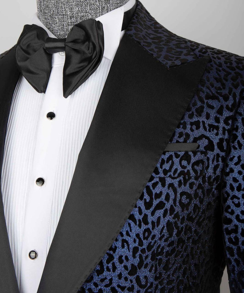 A close-up of a formal tuxedo jacket on a mannequin, featuring a black satin lapel and bow tie over a white pinstripe shirt, with a blue and black leopard-print brocade jacket body.