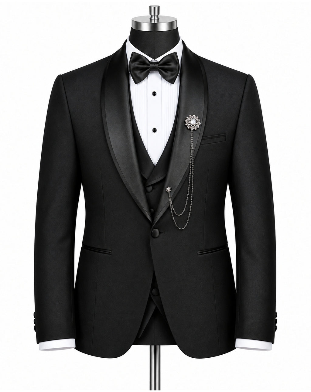 A black tuxedo jacket displayed on a mannequin torso, styled with a black satin shawl collar, a white pleated tuxedo shirt, a black bow tie, a matching black vest, and a decorative brooch with chain detail.