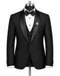 A black tuxedo jacket displayed on a mannequin torso, styled with a black satin shawl collar, a white pleated tuxedo shirt, a black bow tie, a matching black vest, and a decorative brooch with chain detail.