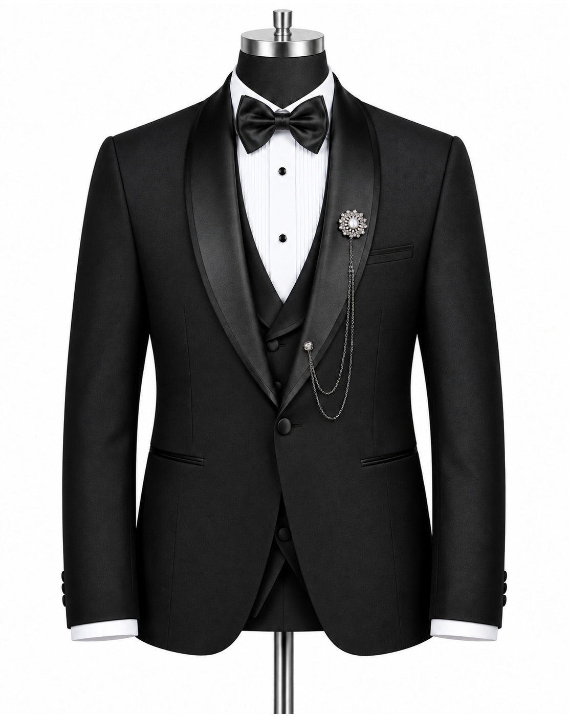 A black tuxedo jacket displayed on a mannequin torso, styled with a black satin shawl collar, a white pleated tuxedo shirt, a black bow tie, a matching black vest, and a decorative brooch with chain detail.