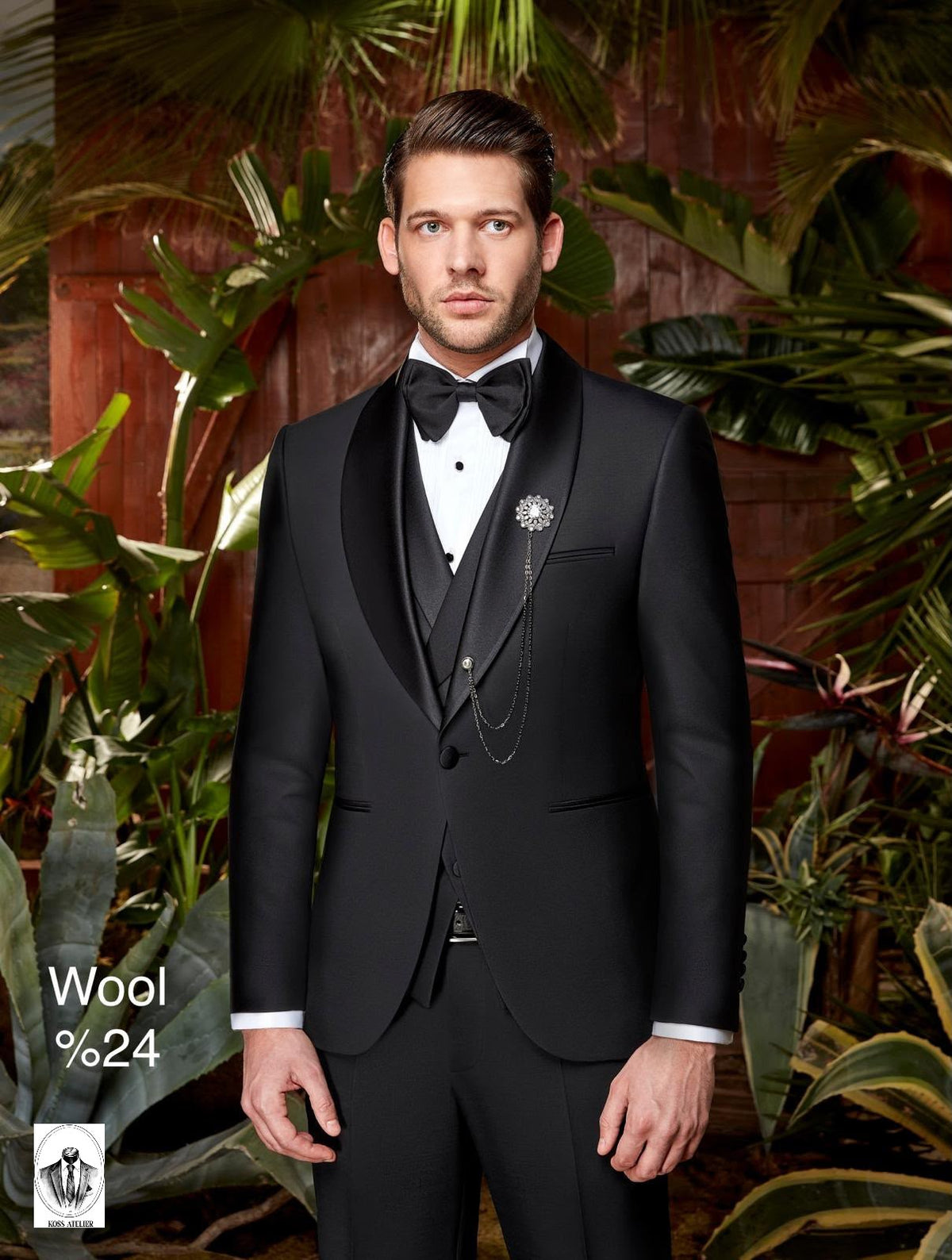 A man wearing a black wool tuxedo with satin lapels, a white dress shirt, a black bow tie, and a decorative brooch, posed in front of a tropical leafy background. Text in the lower left reads 'Wool %24' with a small logo below it.