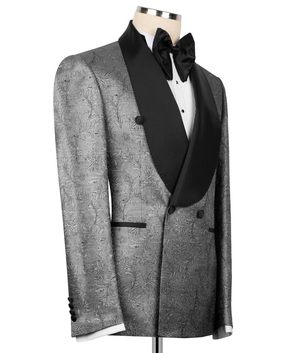 A men's tuxedo jacket displayed on a mannequin torso, featuring a textured silver-gray brocade pattern with black satin shawl lapels, a black bow tie, and a white dress shirt.