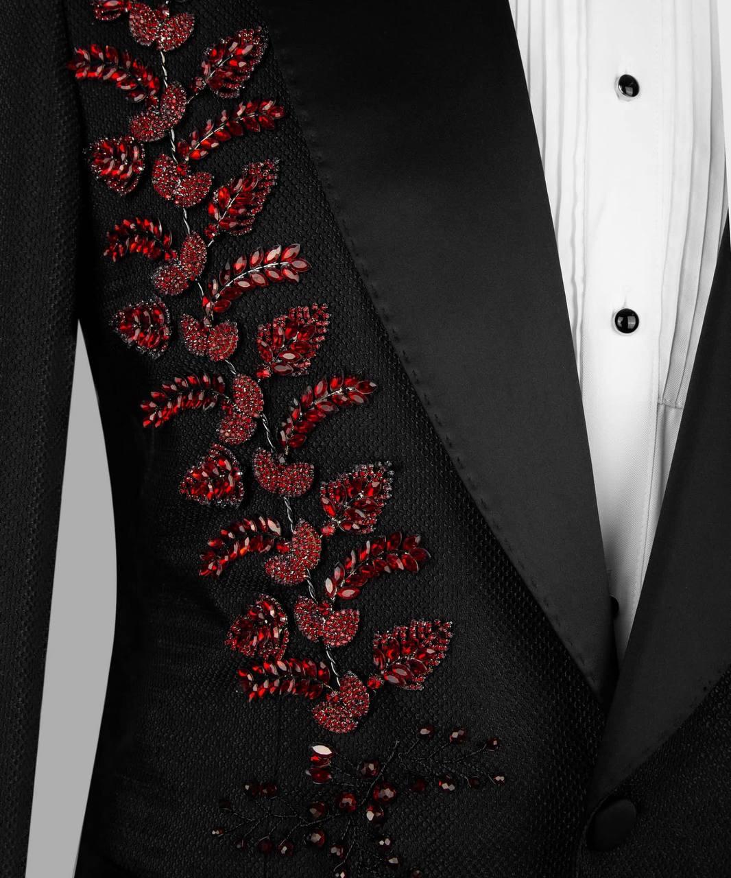 Close-up of a black tuxedo jacket with red beaded leaf embroidery on the lapel, paired with a white pleated tuxedo shirt.