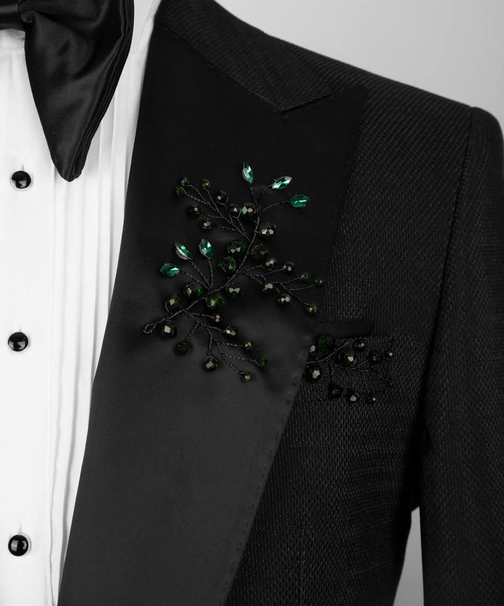 Black suit jacket with decorative green brooch on a white background