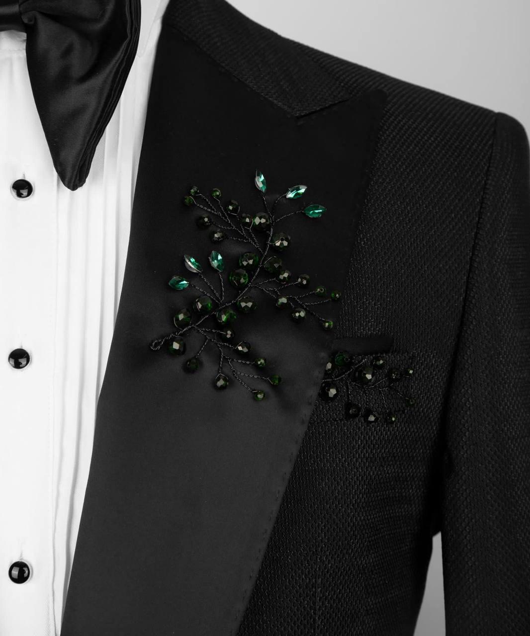 Black suit jacket with decorative green brooch on a white background