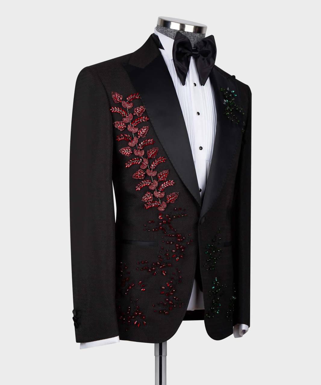 A black tuxedo jacket with satin lapels and elaborate red, green, and blue beaded floral embroidery down the front, displayed on a mannequin with a white shirt and black bow tie.