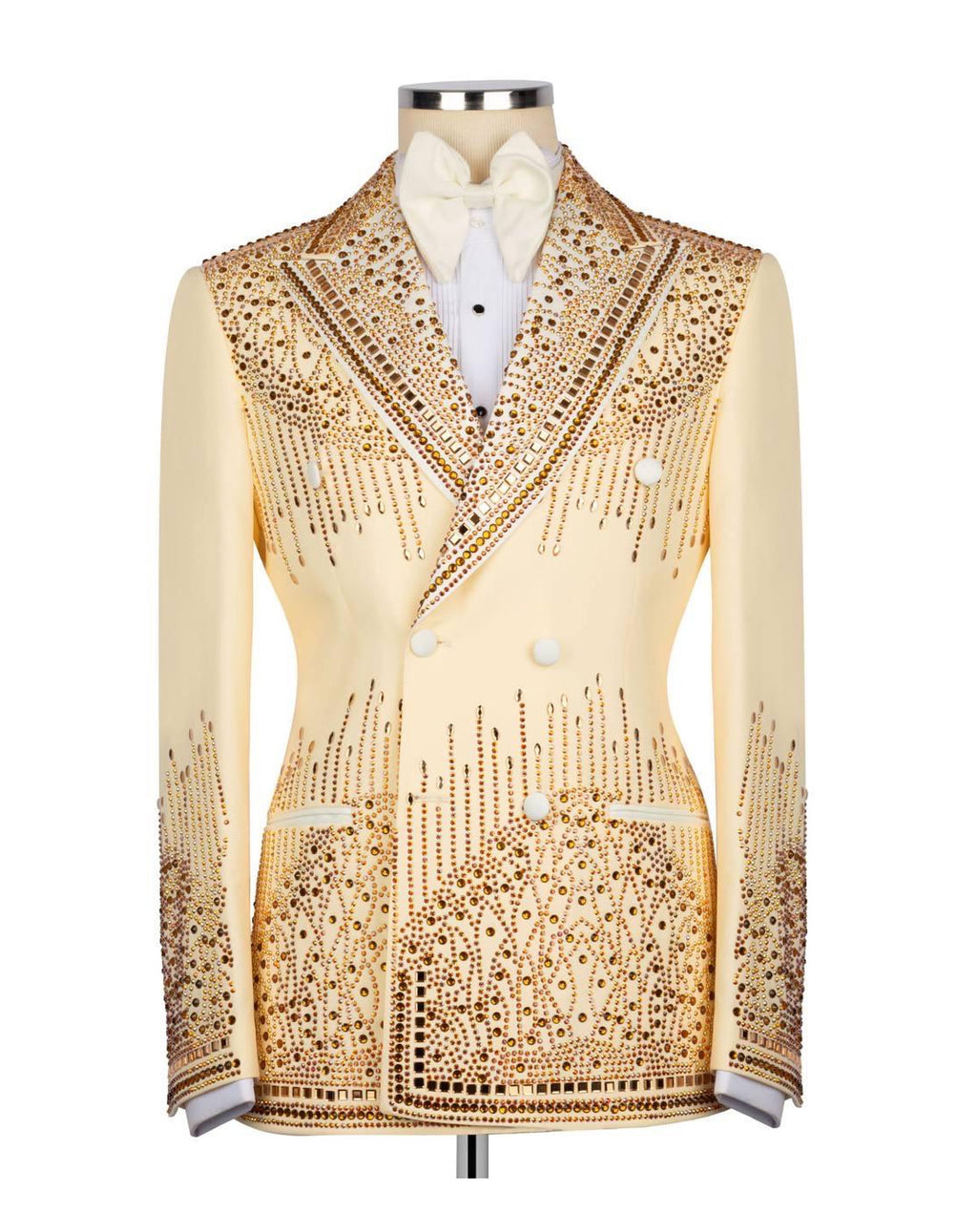A cream-colored double-breasted tuxedo jacket heavily embellished with gold rhinestones and beadwork, displayed on a mannequin with a white shirt and bow tie.
