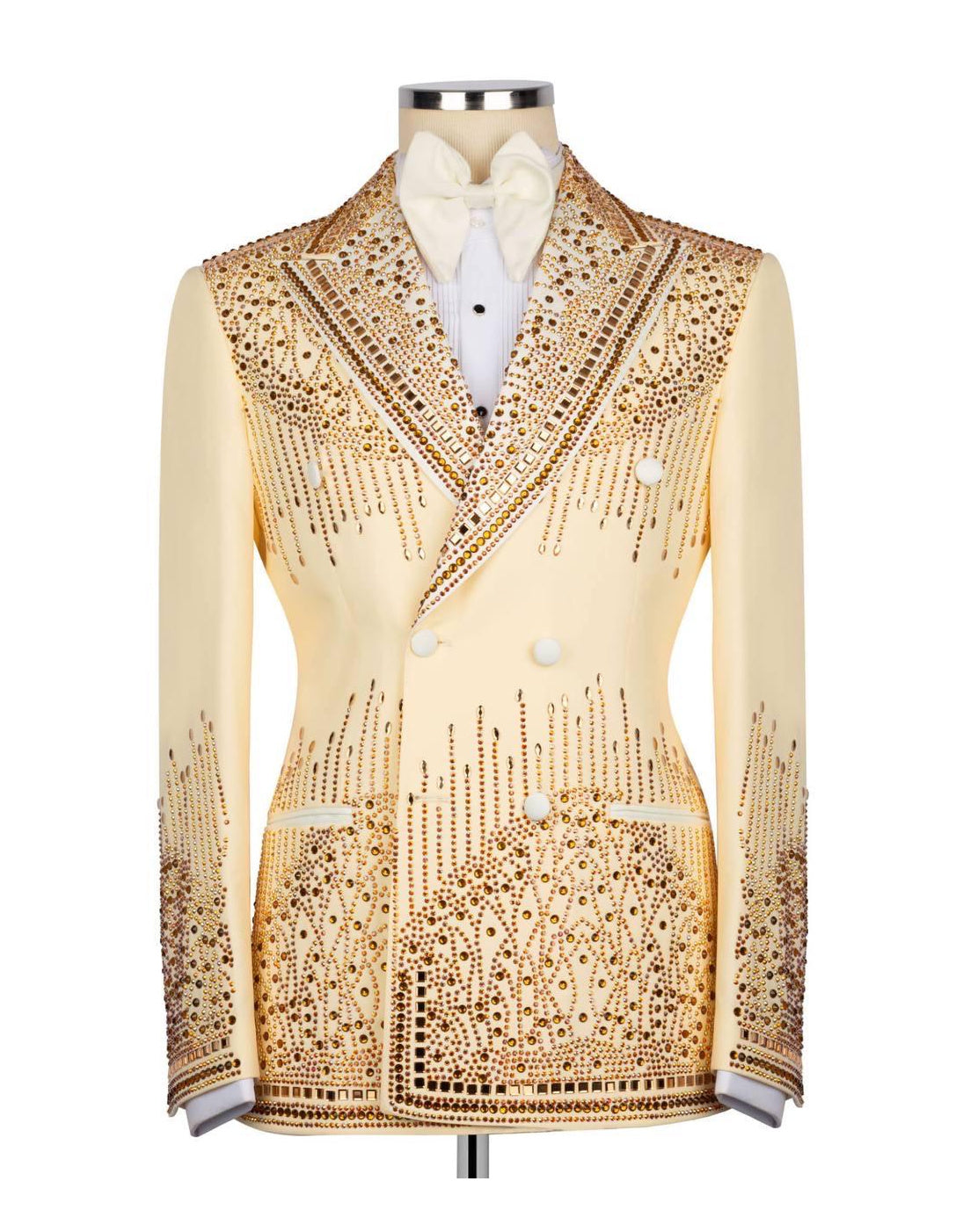A cream-colored double-breasted tuxedo jacket heavily embellished with gold rhinestones and beadwork, displayed on a mannequin with a white shirt and bow tie.