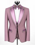 A men's formal suit displayed on a mannequin, featuring a dusty pink blazer with satin lavender lapels and trim, a matching vest, a white dress shirt, a lavender bow tie, and a matching lavender waistcoat.