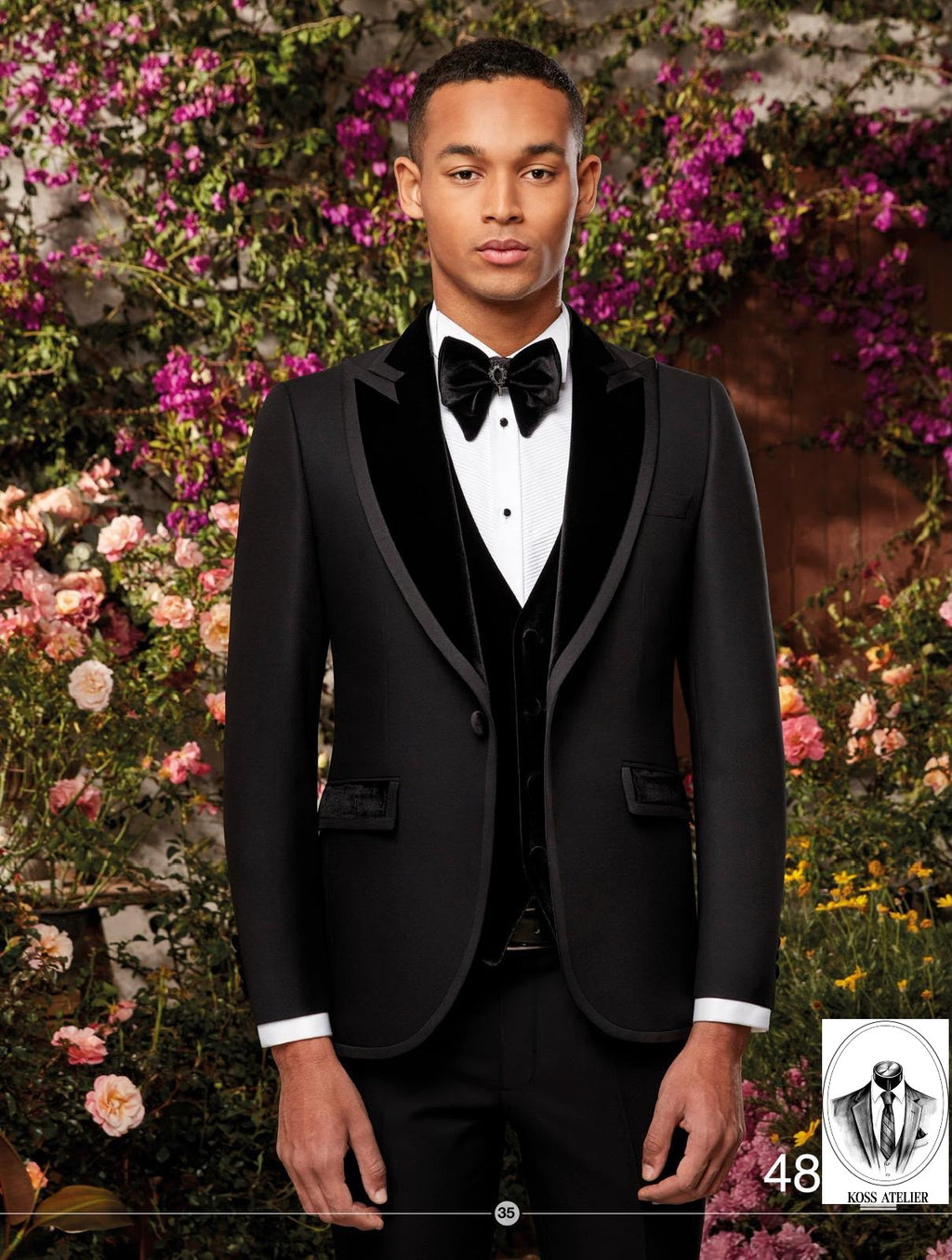A man wearing a black tuxedo jacket with black velvet lapels, a black vest, a white dress shirt, and a black bow tie, standing in front of a lush background of pink and white flowers.