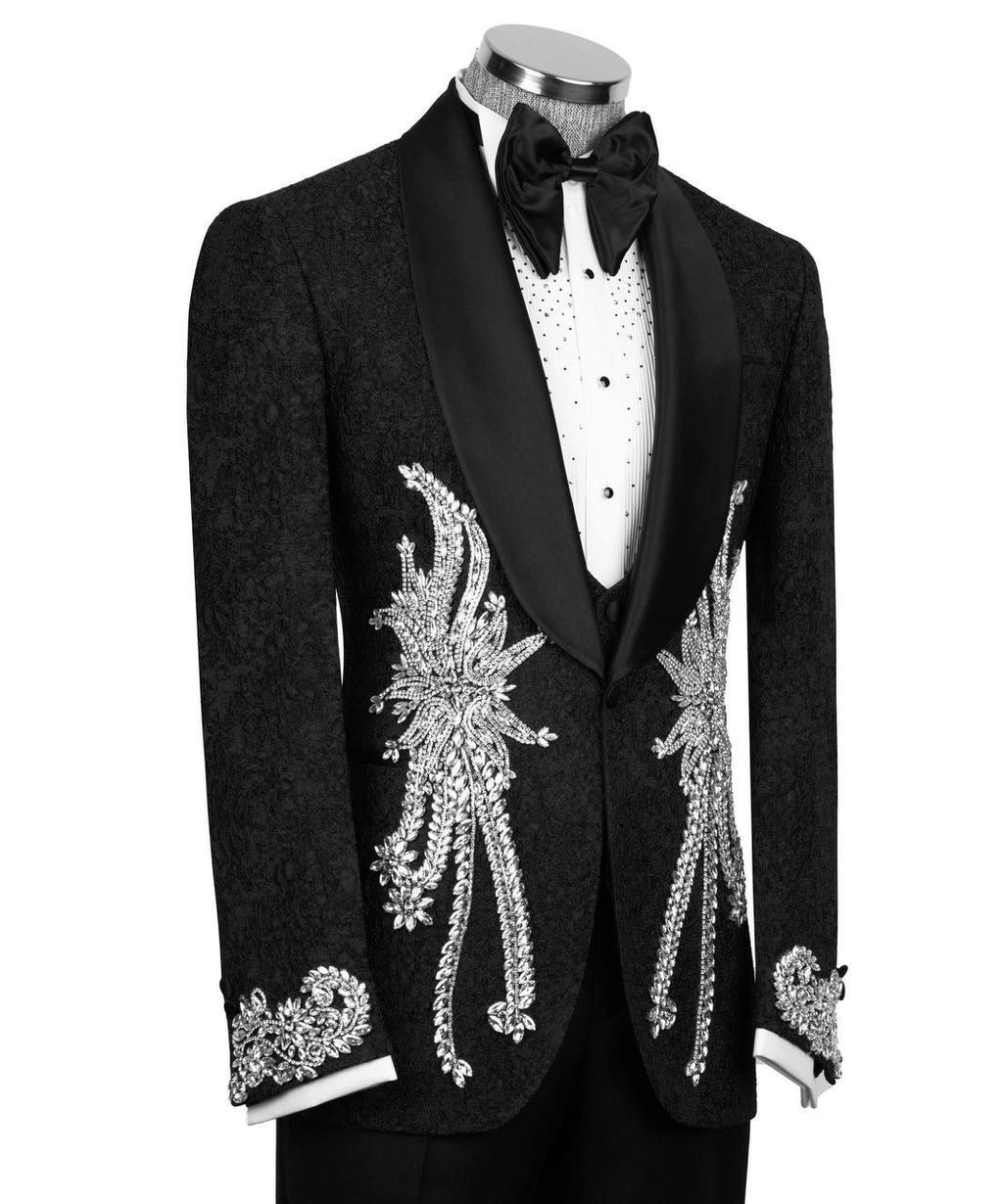 A black tuxedo jacket with ornate silver crystal embellishments on the front and cuffs, styled on a mannequin with a white patterned shirt and black bow tie against a white background.