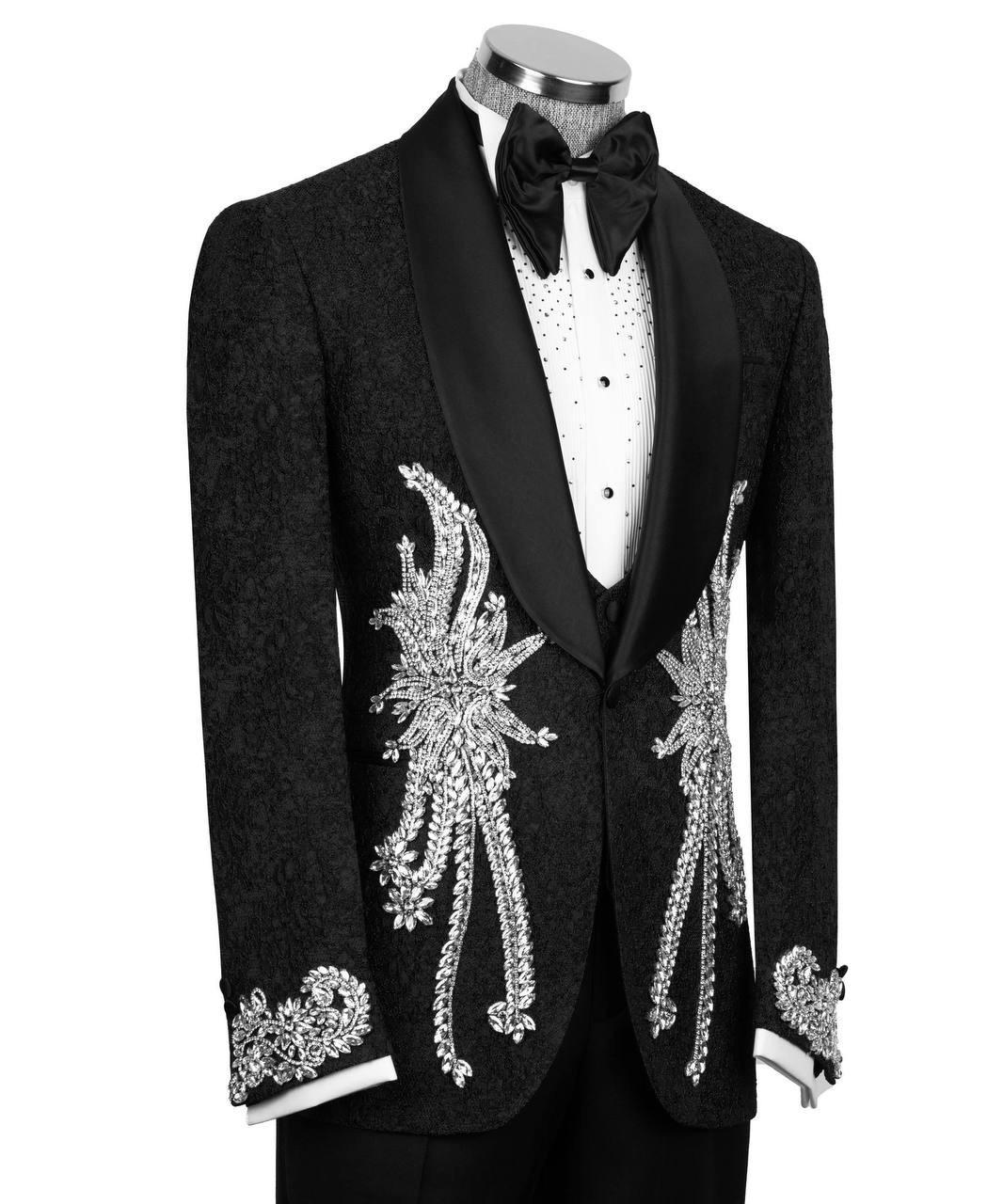 A black tuxedo jacket with ornate silver crystal embellishments on the front and cuffs, styled on a mannequin with a white patterned shirt and black bow tie against a white background.