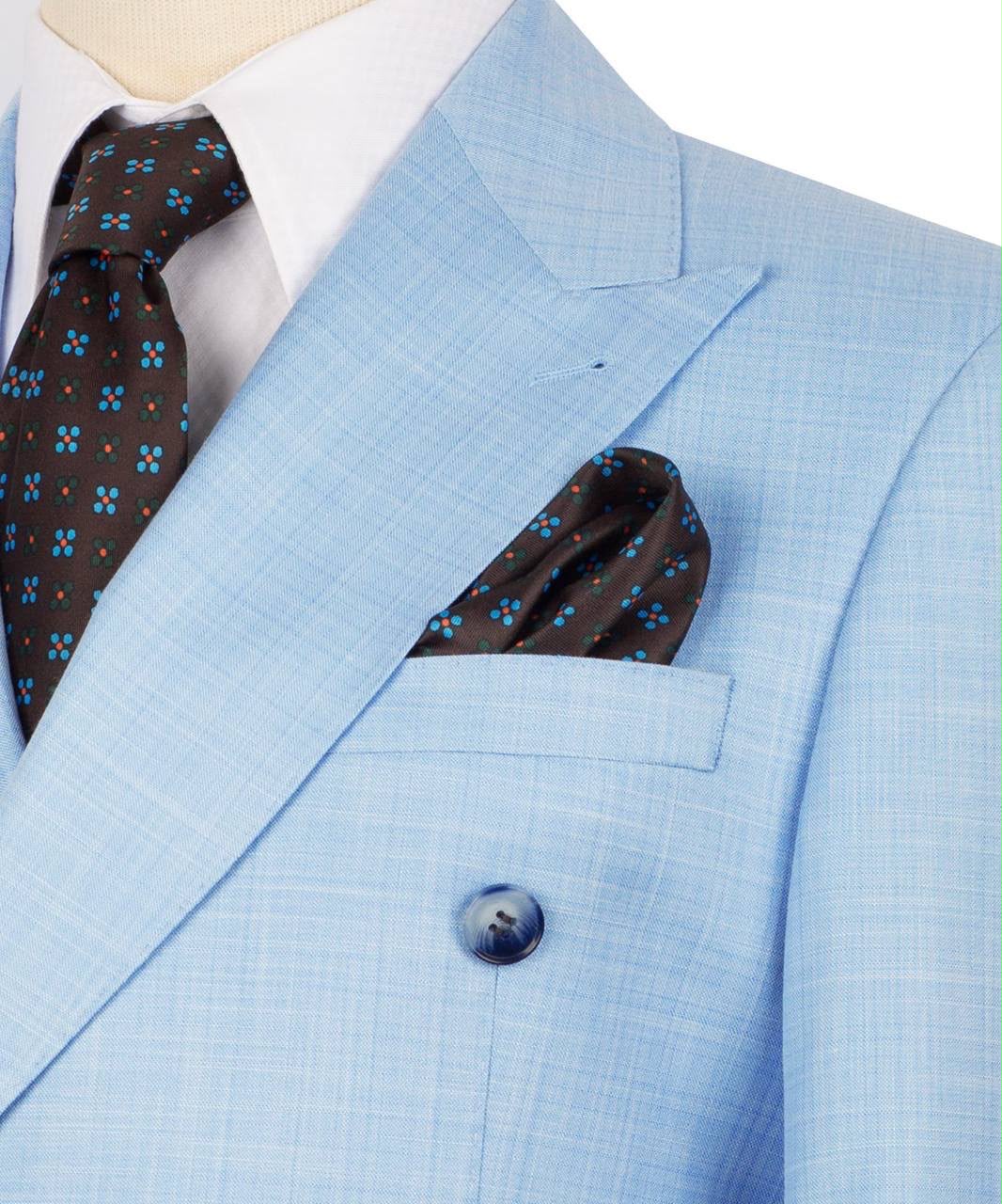 A close-up of a light blue double-breasted suit jacket with a subtle windowpane texture, styled with a white dress shirt, a dark brown patterned tie, and a matching pocket square.