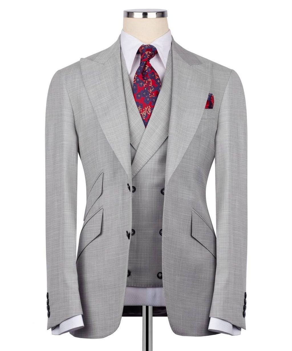 A light gray three-piece suit displayed on a mannequin, featuring a double-breasted jacket, matching vest, and trousers, styled with a white dress shirt, a red and blue paisley tie, and a matching pocket square.