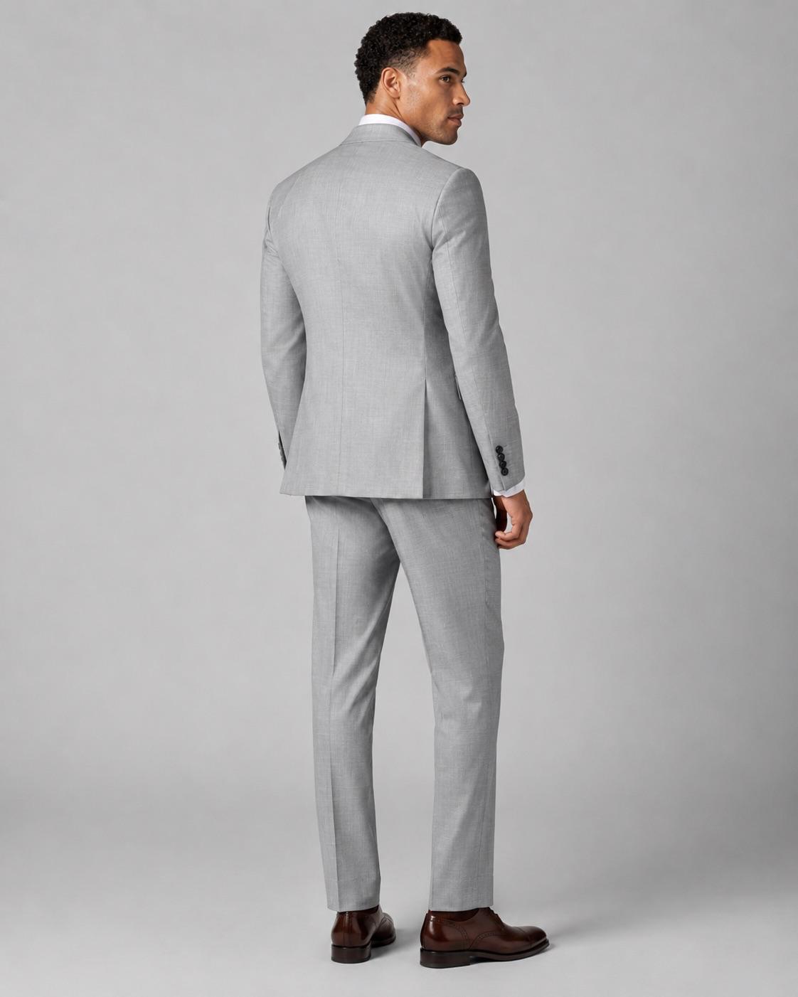 A man wearing a light gray two-piece suit, shown from the back, standing against a solid gray studio background.