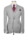 A light gray three-piece suit displayed on a mannequin, styled with a white dress shirt, a red and blue paisley patterned tie, and a matching pocket square.