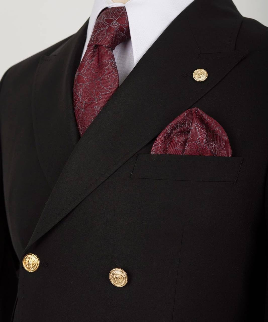 Close-up of a double-breasted black suit jacket with gold buttons, a white dress shirt, a burgundy patterned tie, and a matching burgundy pocket square.