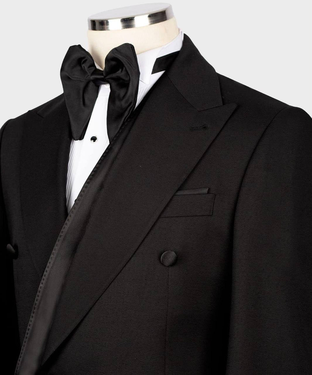 A black double-breasted tuxedo jacket displayed on a mannequin torso, paired with a white dress shirt, black bow tie, and black satin lapel trim