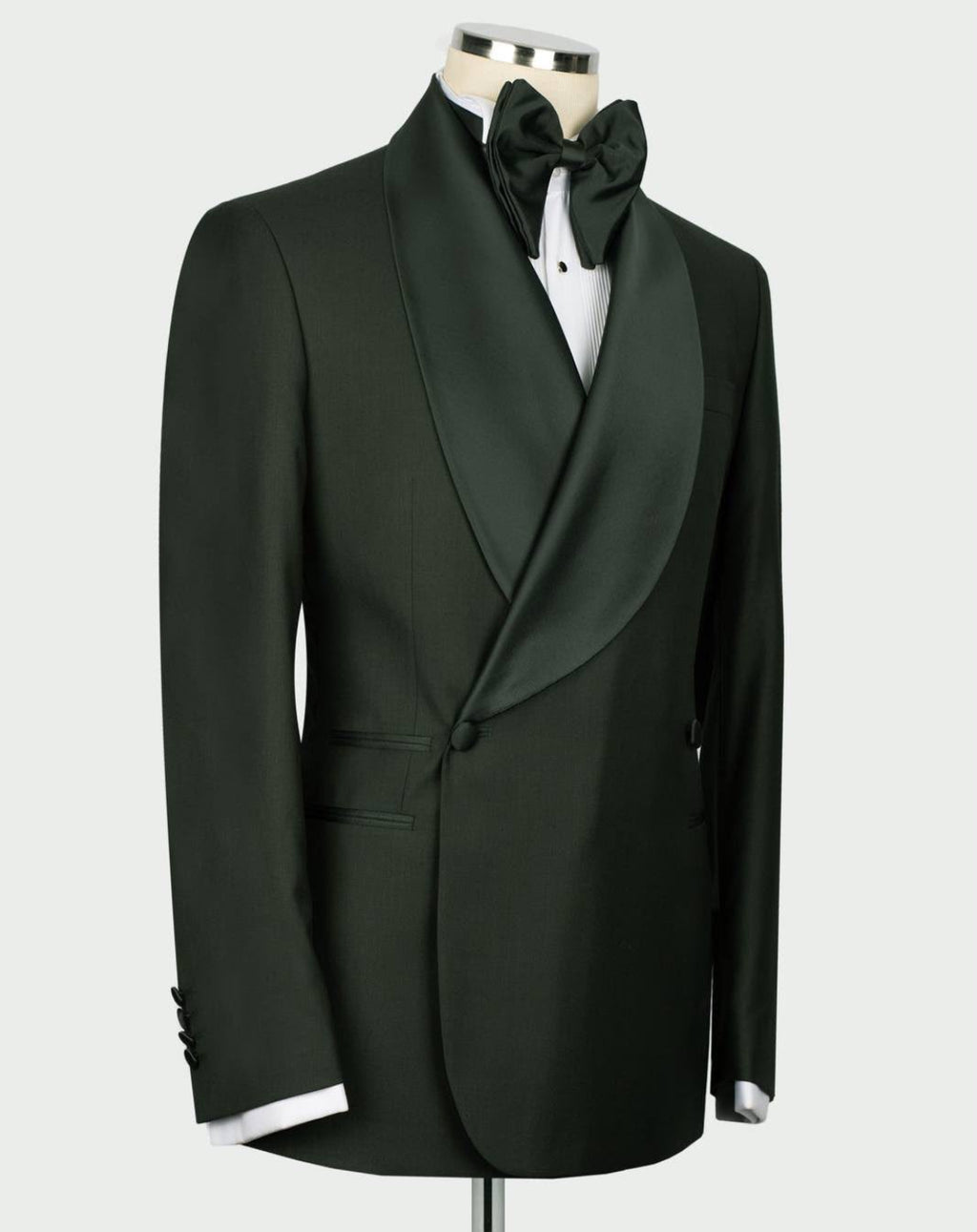 A dark forest green double-breasted tuxedo jacket with satin peak lapels, styled on a mannequin with a matching green bow tie