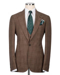 A brown plaid suit jacket displayed on a mannequin torso, styled with a white dress shirt, a green patterned tie, and a matching pocket square
