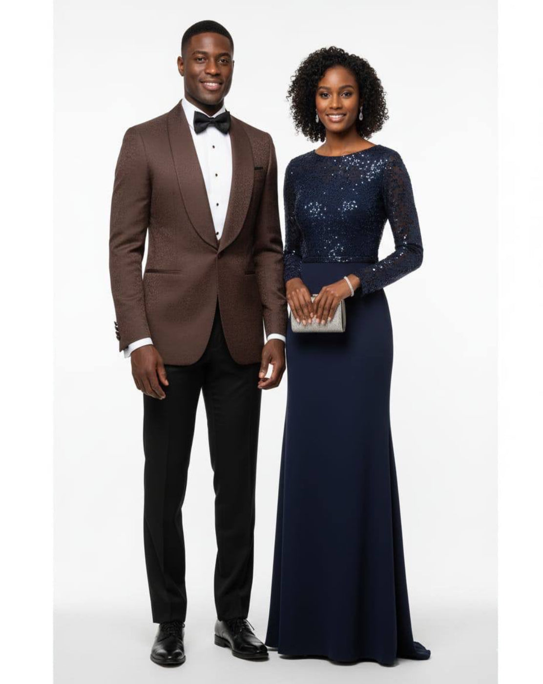A man in a brown tuxedo with a black bow tie and black trousers stands next to a woman in a navy blue sequined floor-length gown holding a silver clutch, 