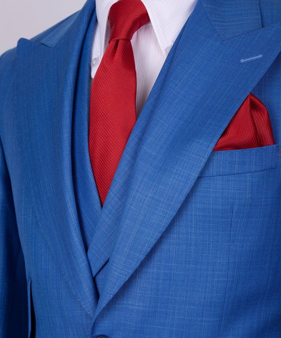 Blue suit with a red tie and pocket square on a light gray background