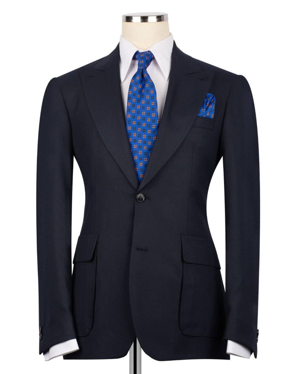 A dark navy blue suit jacket displayed on a mannequin torso, styled with a white dress shirt, a blue patterned tie, and a matching blue patterned pocket square against a plain white background.