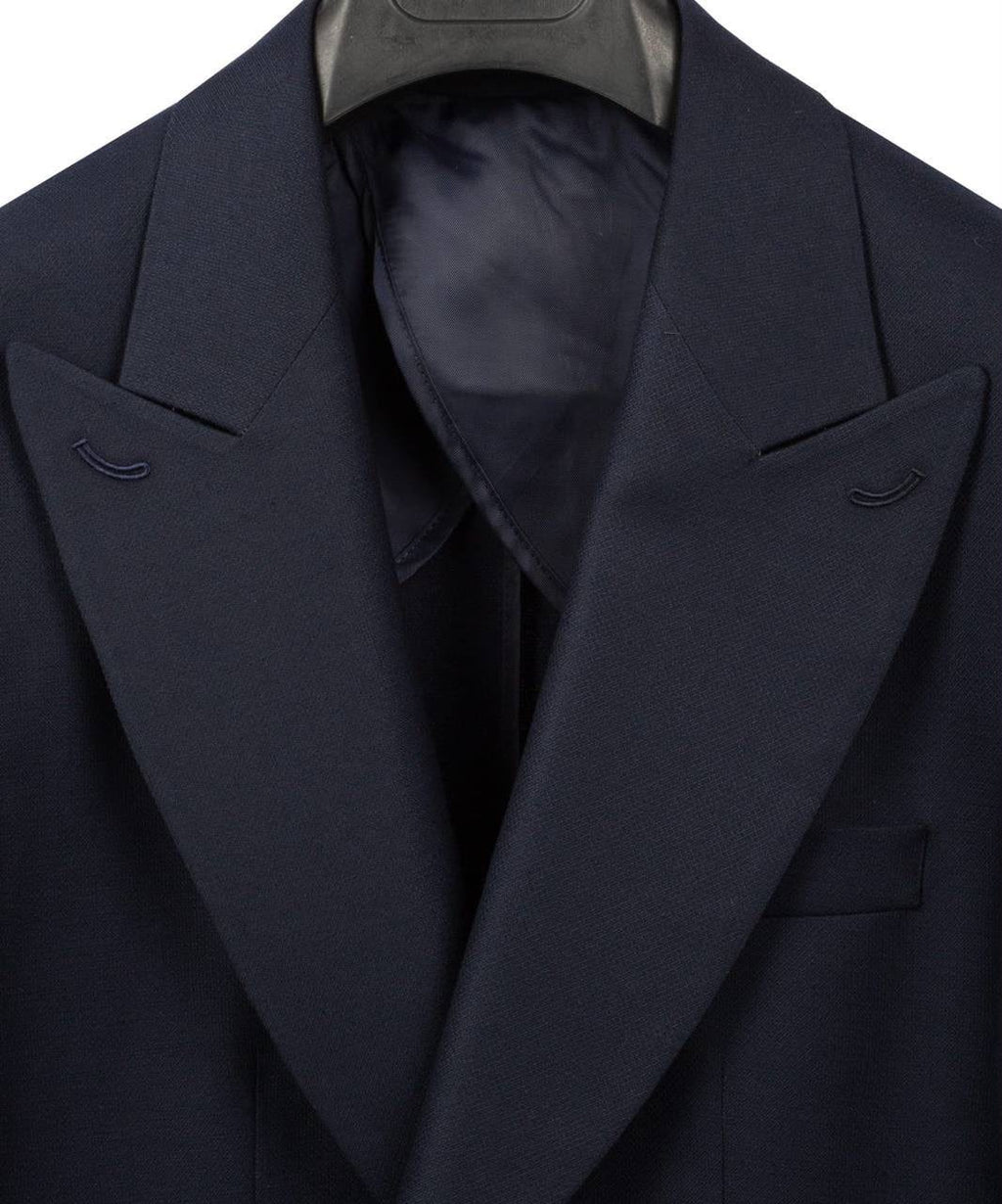 Close-up of a dark navy blue suit jacket with wide notched lapels and a matching dark satin inner collar, shown on a hanger against a white background.