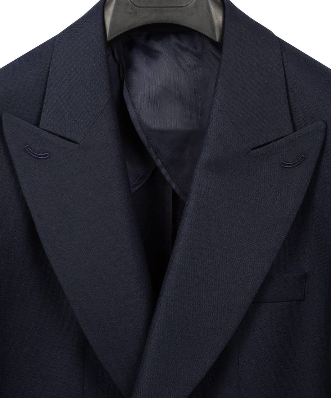 Close-up of a dark navy blue suit jacket with wide notched lapels and a matching dark satin inner collar, shown on a hanger against a white background.
