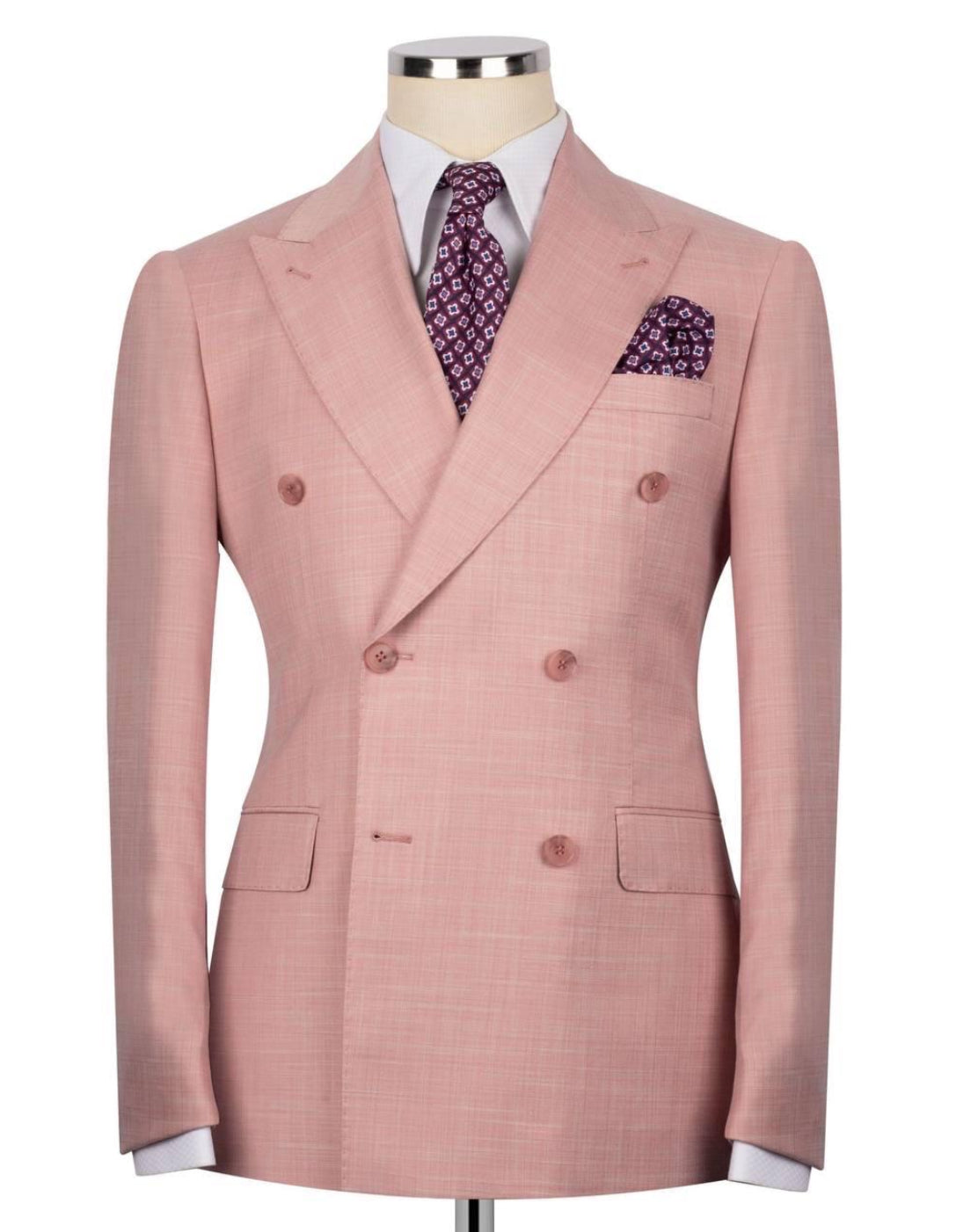 A men's double-breasted suit jacket in a light pink fabric, displayed on a mannequin torso with a white dress shirt, a purple patterned tie, and a matching pocket square.