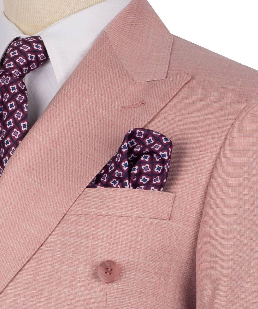 A close-up of a men's suit featuring a dusty pink double-breasted blazer with a subtle grid pattern, styled with a white dress shirt, a patterned burgundy tie, and a matching pocket square.