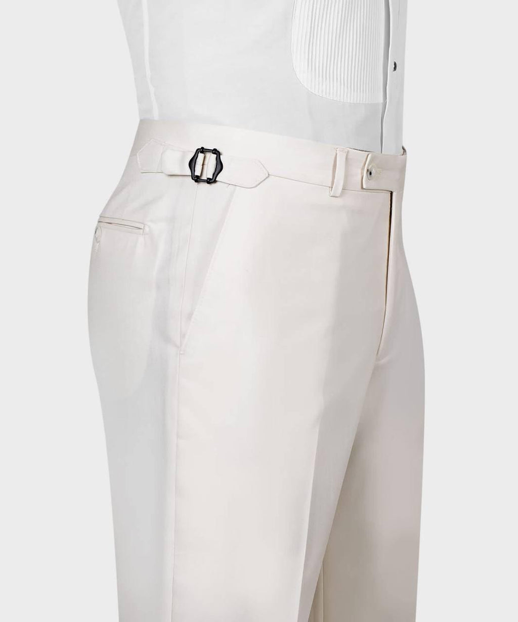 Close-up of a person wearing light cream trousers with a matching belt featuring a black metal buckle, paired with a white pleated shirt against a light gray background.