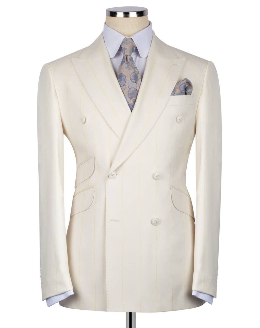 A cream-colored double-breasted suit jacket with subtle vertical pinstripes, displayed on a mannequin torso with a light blue dress shirt, a patterned blue and gold tie, and a matching pocket square.
