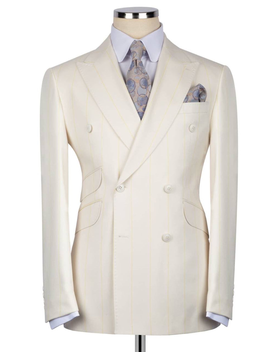 A cream-colored double-breasted suit jacket with subtle vertical pinstripes, displayed on a mannequin torso with a light blue dress shirt, a patterned blue and gold tie, and a matching pocket square.