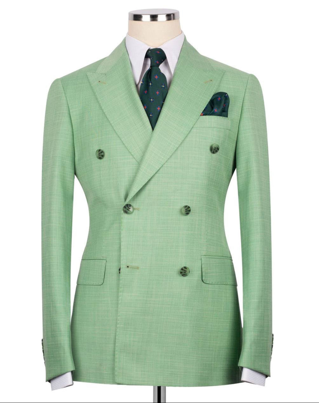 A light green double-breasted suit jacket with a subtle windowpane pattern, displayed on a mannequin torso with a white dress shirt, a green patterned tie, and a matching pocket square.