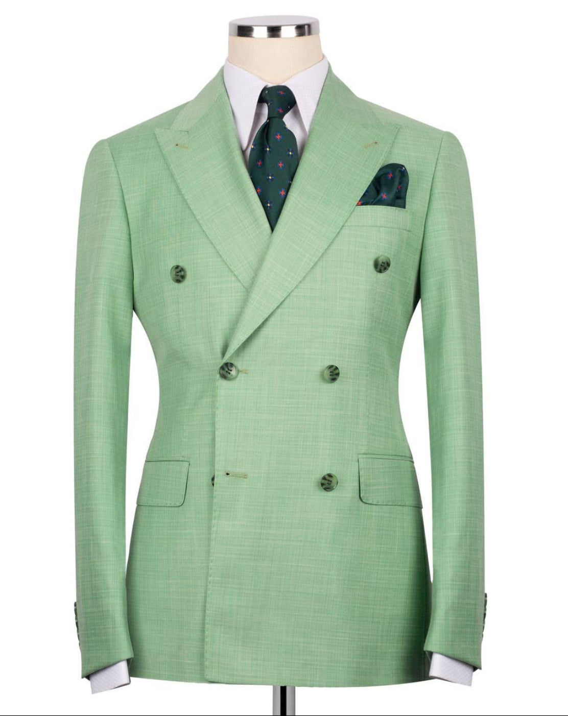 A light green double-breasted suit jacket with a subtle windowpane pattern, displayed on a mannequin torso with a white dress shirt, a green patterned tie, and a matching pocket square.