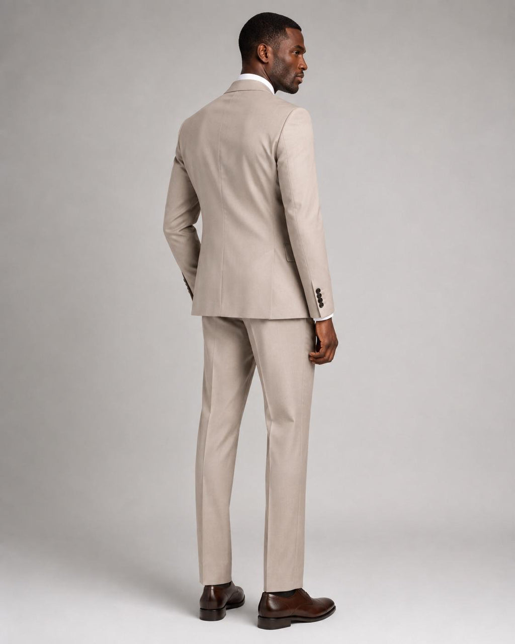 A man wearing a light beige two-piece suit, shown from a rear three-quarter angle against a neutral gray studio background.