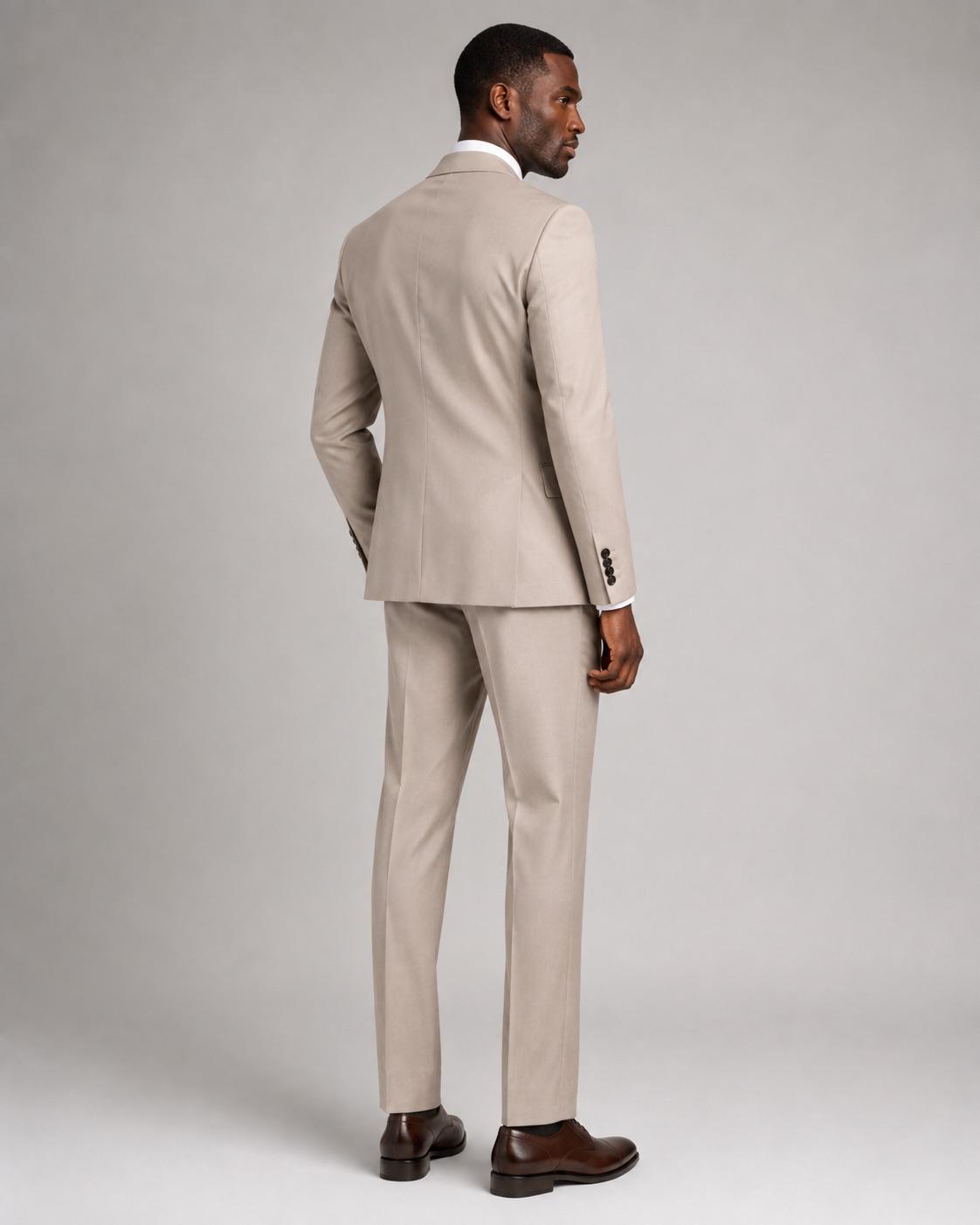 A man wearing a light beige two-piece suit, shown from a rear three-quarter angle against a neutral gray studio background.