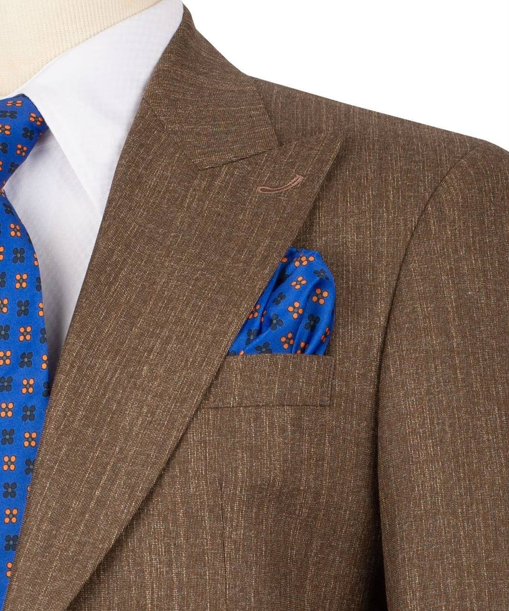A close-up of a brown textured suit jacket worn with a white dress shirt, a blue patterned tie, and a matching blue pocket square with orange and black floral motifs.